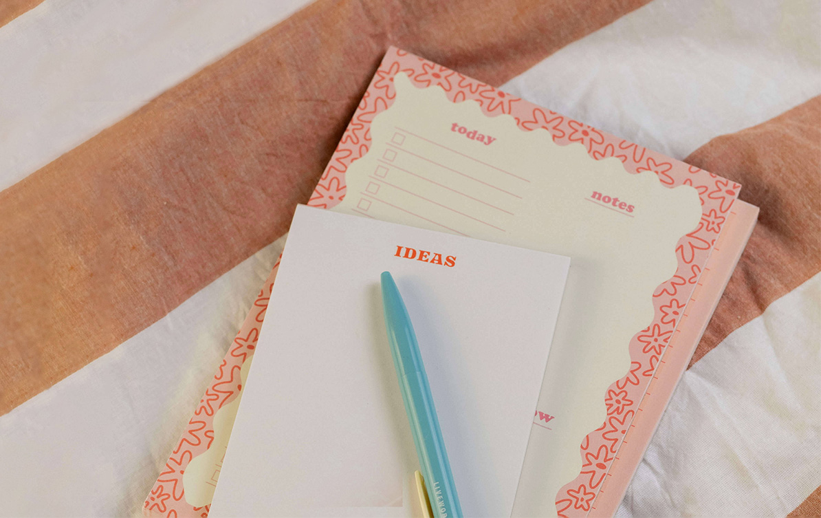 A notebook, pen, and notepad neatly arranged on a bed. Perfect tools for jotting down ideas.